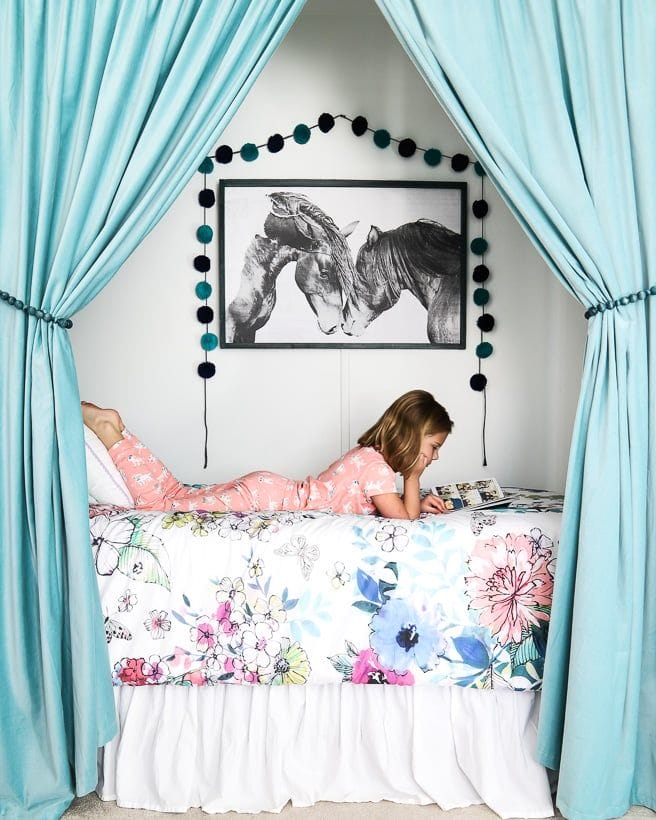 dormitor tineret cu un copil citind pe pat alb si draperii turcoaz deschis